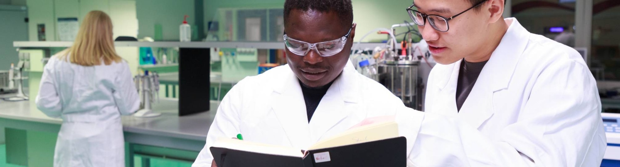 Studenten master Life Sciences Alain Barhasima en Dat Le werken in een biologielab. Op de rug Lisan Scholten