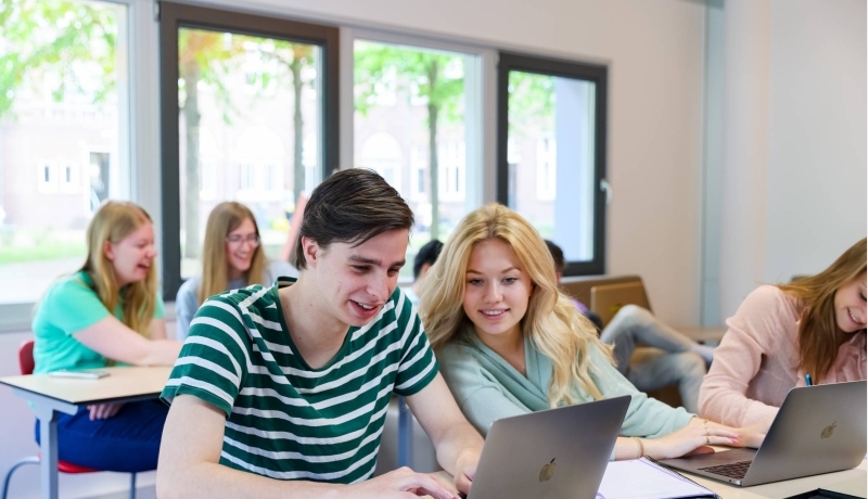 meerdere studenten van bedrijfskunde in een klaslokaal, twee studenten kijken naar een laptop