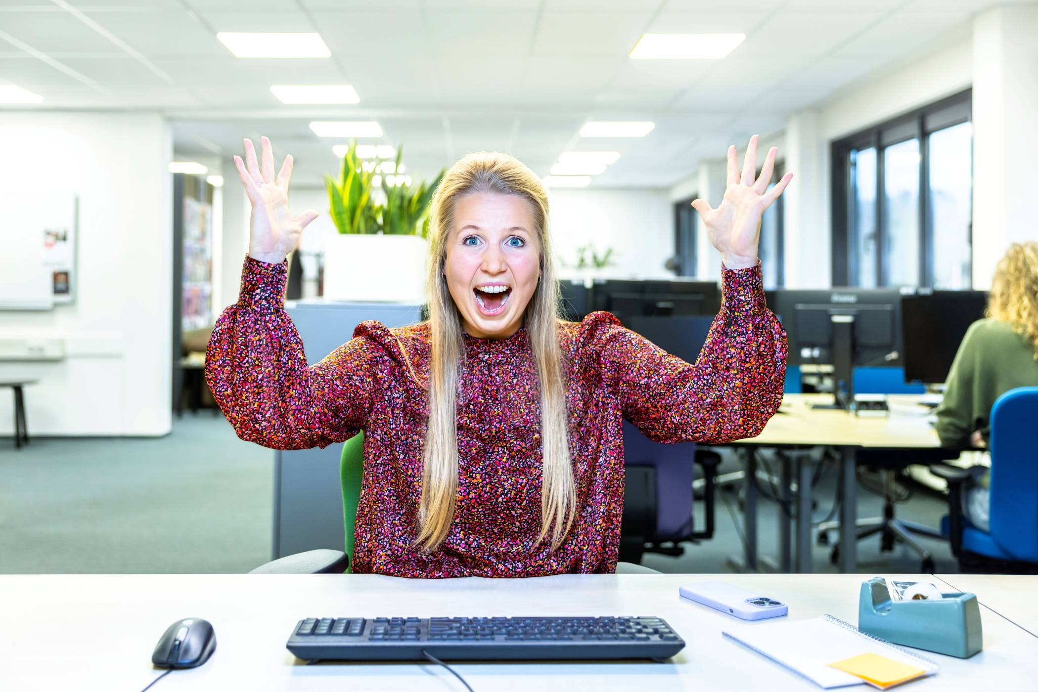 Cursist achter een bureau lacht en steekt armen juichend in de lucht.