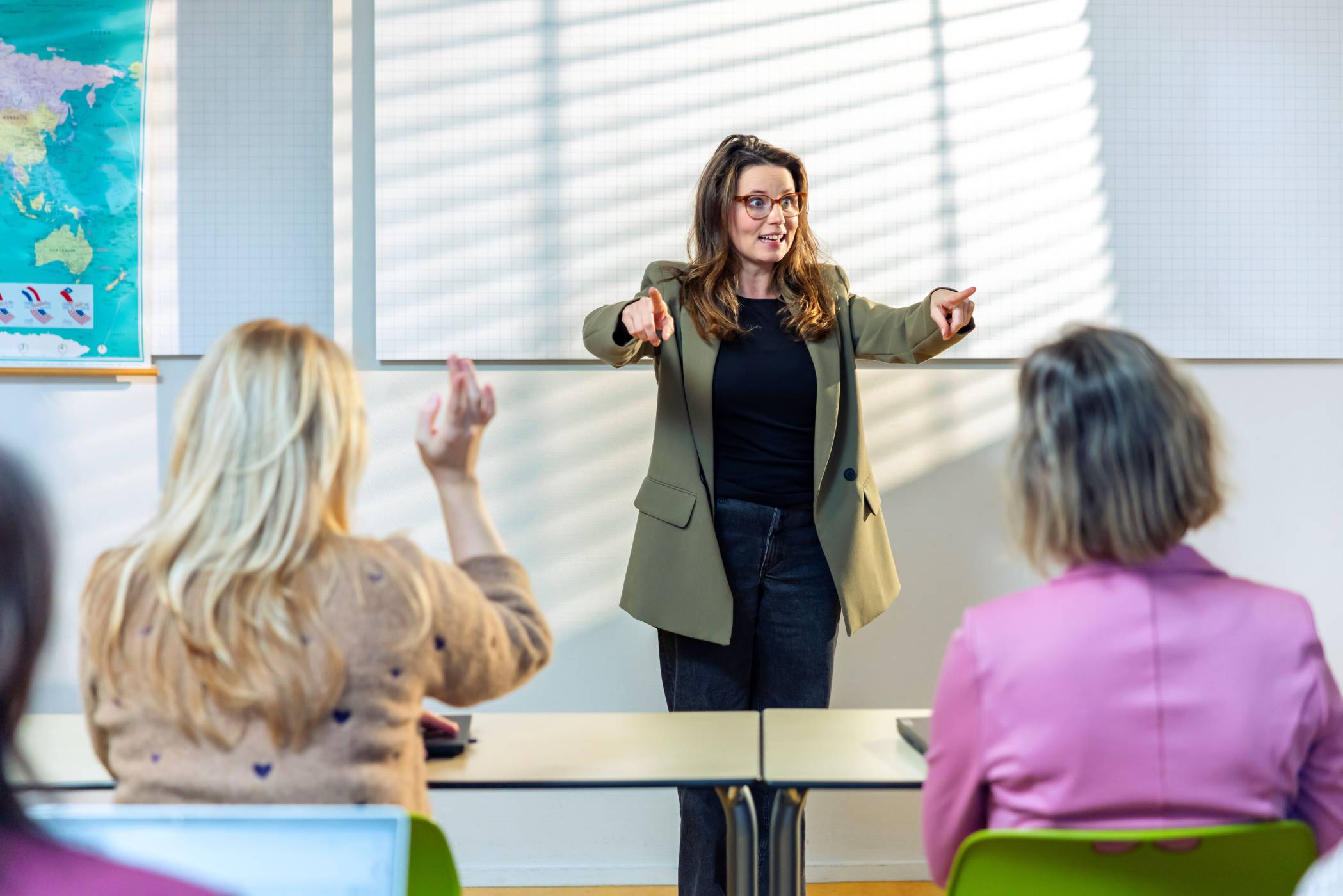 Cursist achter een bureau lacht en steekt armen juichend in de lucht.