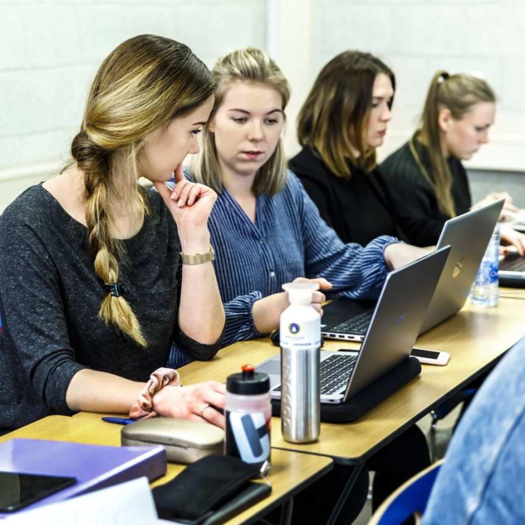 drie studenten ad bedrijfskunde kijken met elkaar mee op laptop in klaslokaal