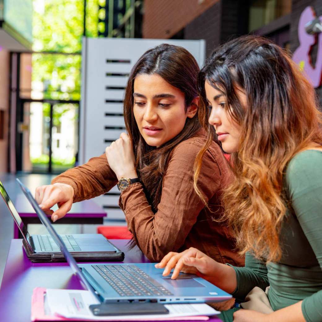 2 bachelor studenten overleggen bij een laptop op de campus.