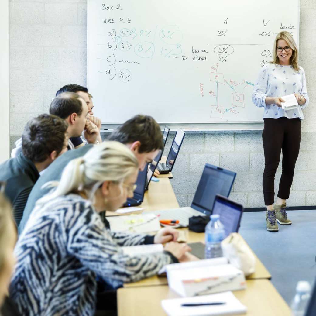 Docent geeft les aan deeltijd studenten die achter laptop zitten op de opleiding associate degree logistiek deeltijd