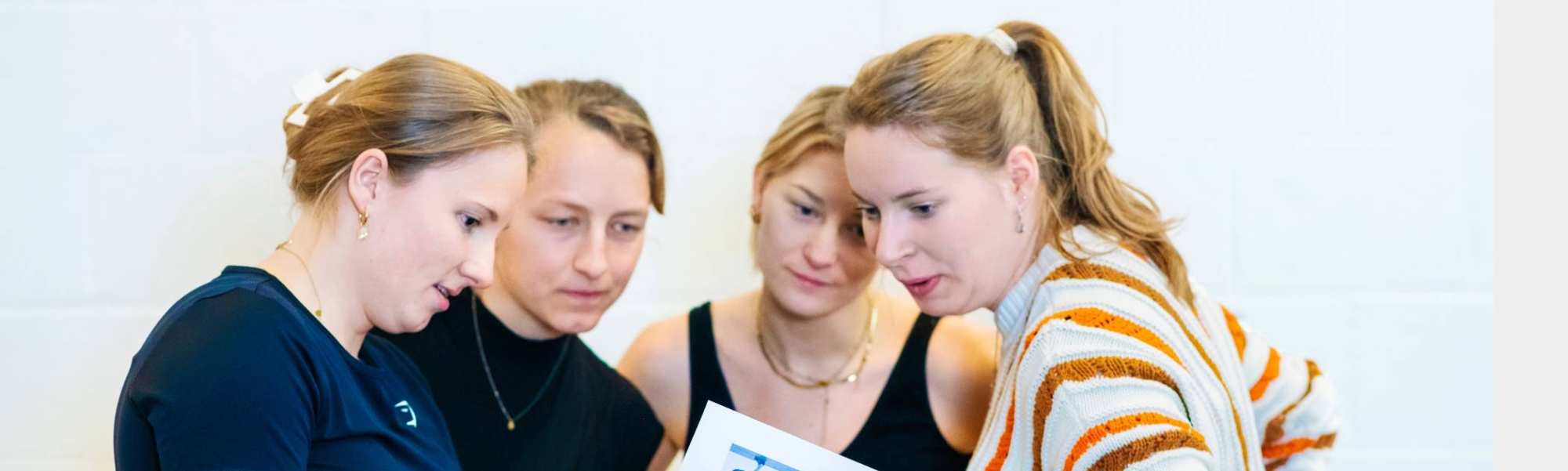 4 vrouwelijke studenten bekijken een oefening op papier.