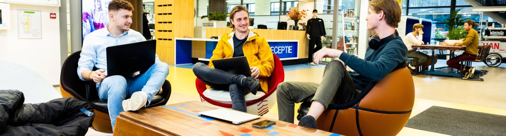 Stagiairs kletsen op draaistoelen in hal Gymnasion.