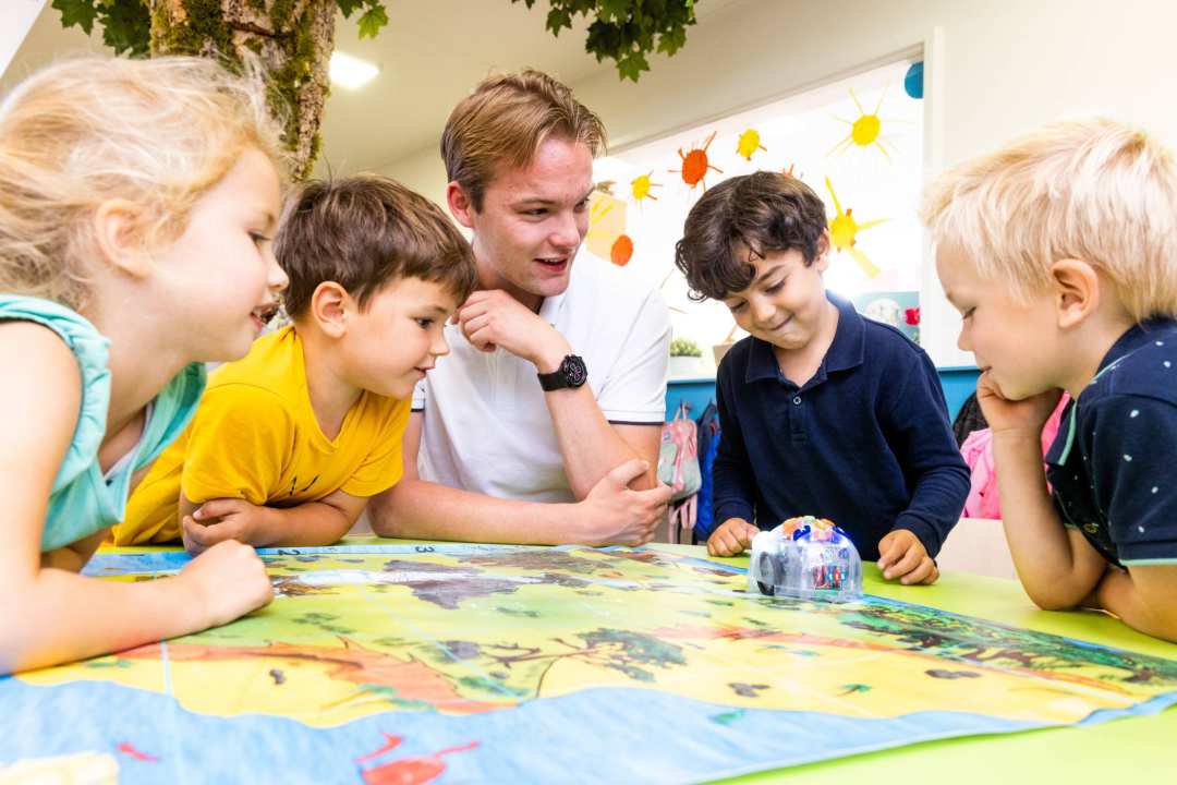 Vier kinderen en een leraar van de opleiding leraar basisonderwijs spelen samen een bordspel in de klas