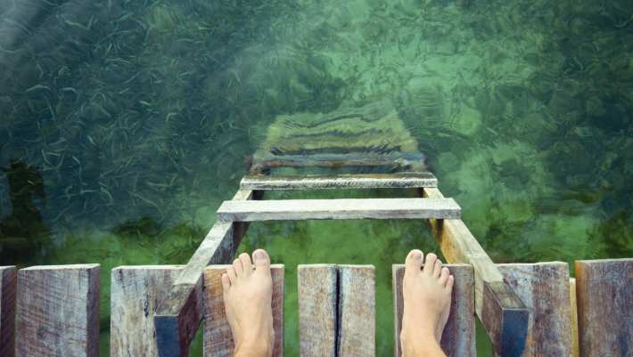 stockfoto van voeten op een vlonder aan de rand van groen water