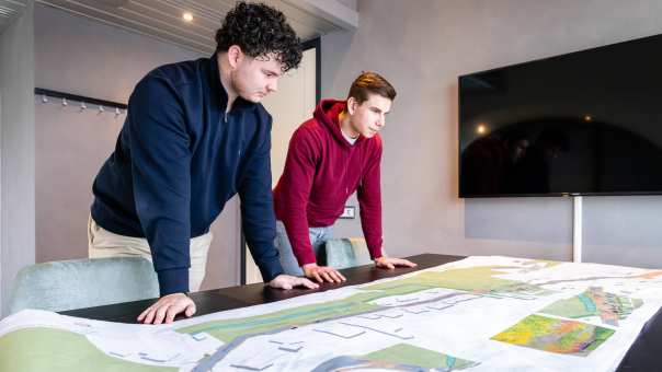 Twee mannen leunen op een bureau met daarop een omgevingskaart.