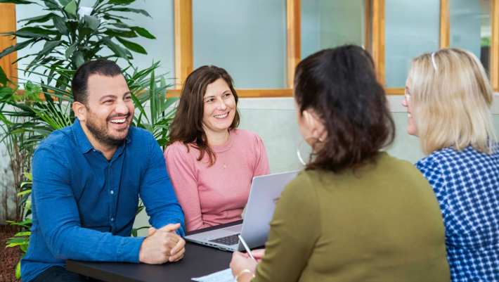Drie master studentes zitten lachend aan tafel.