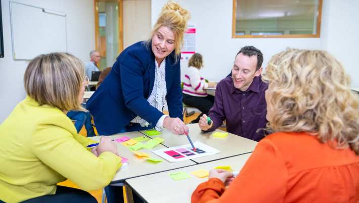 Een groepje van vier mensen in gesprek met post-its op tafel in een lokaal met anderen