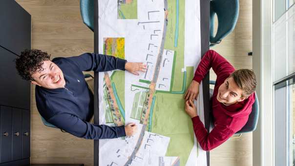 Twee mannen kijken recht omhoog in de camera met een omgevingskaart tussen hen in.