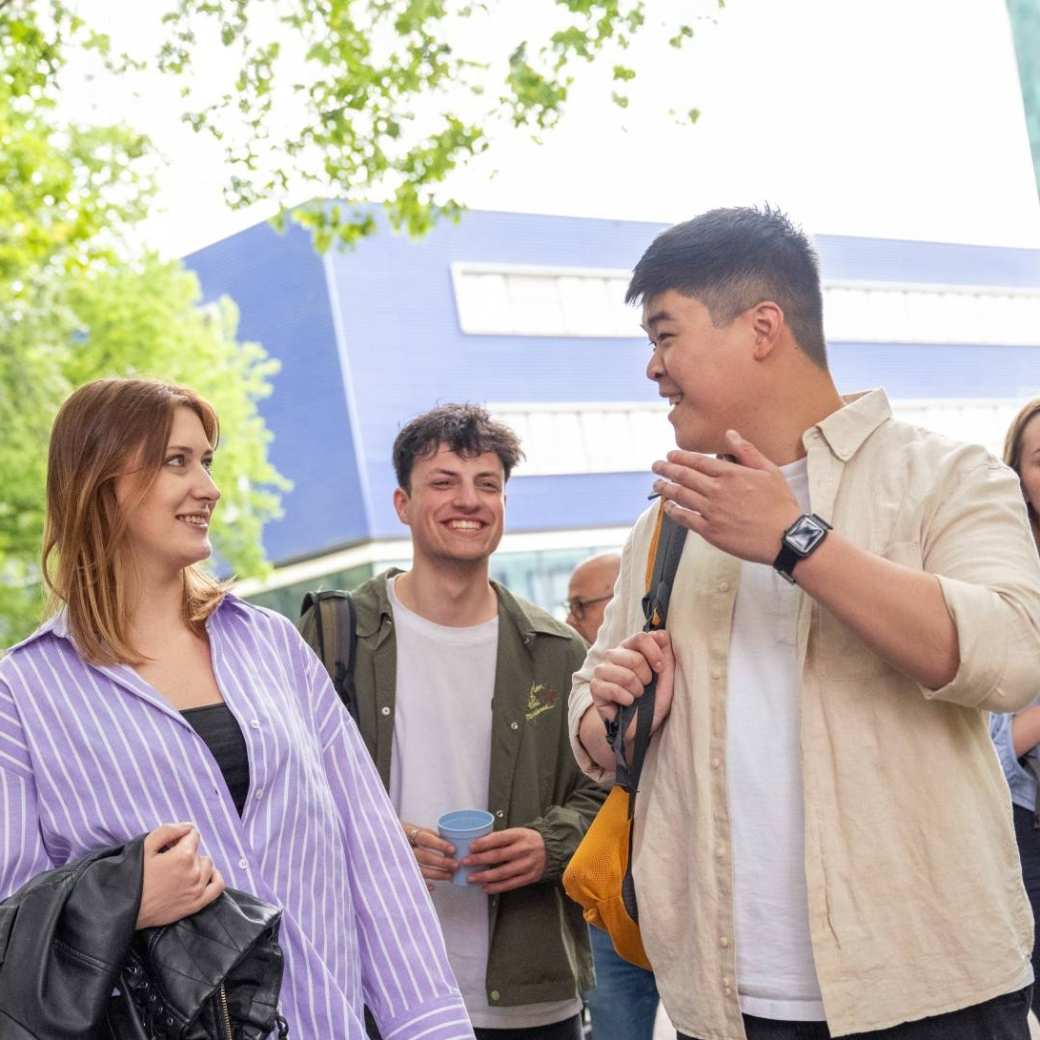 Groepje studenten staan buiten, met elkaar aan het kletsen, op de campus.