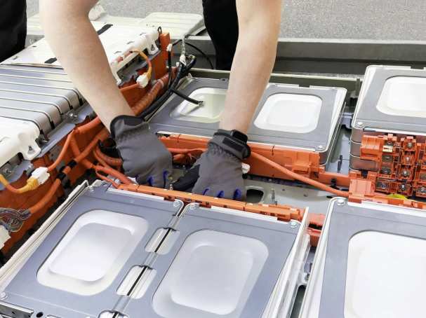 Monteur met blauwe handschoen knutselt aan een grote batterij. Seece - SEE- elektrotechniek, werktuigbouwkunde