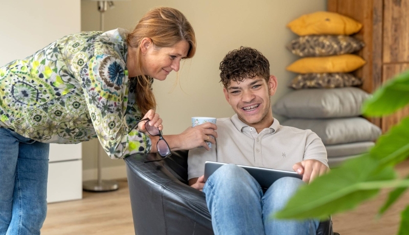 Moeder en zoon lachen terwijl ze hangen in een stoel en bezig zijn op de laptop.