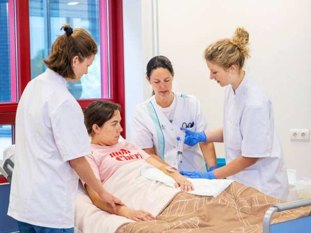 Docent kijkt mee met studenten die bezig zijn met oefenen wondverzorging