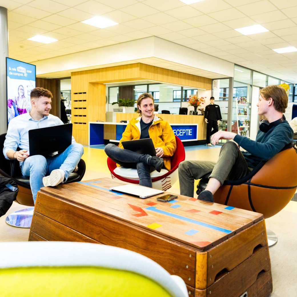 Stagiairs kletsen op draaistoelen in hal Gymnasion.