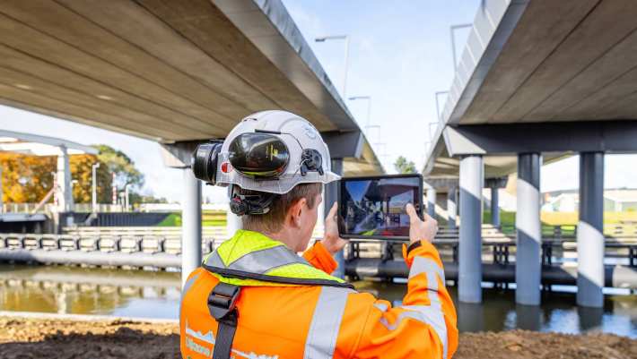 Man met veiligheidshelm en oranje werkjas fotografeert van onderen twee viaducten in aanbouw