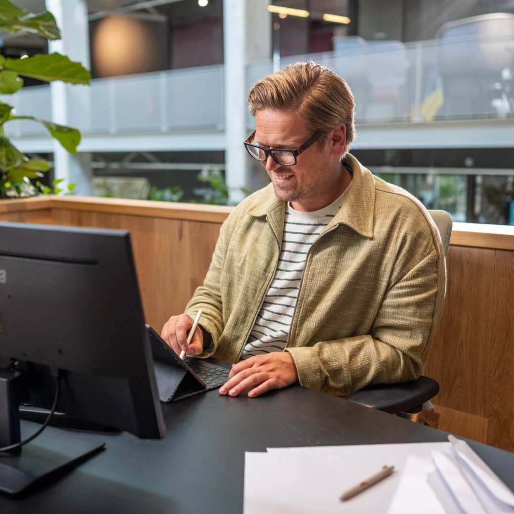 Man met bril op het werk achter een bureau aan het tekenen op tablet