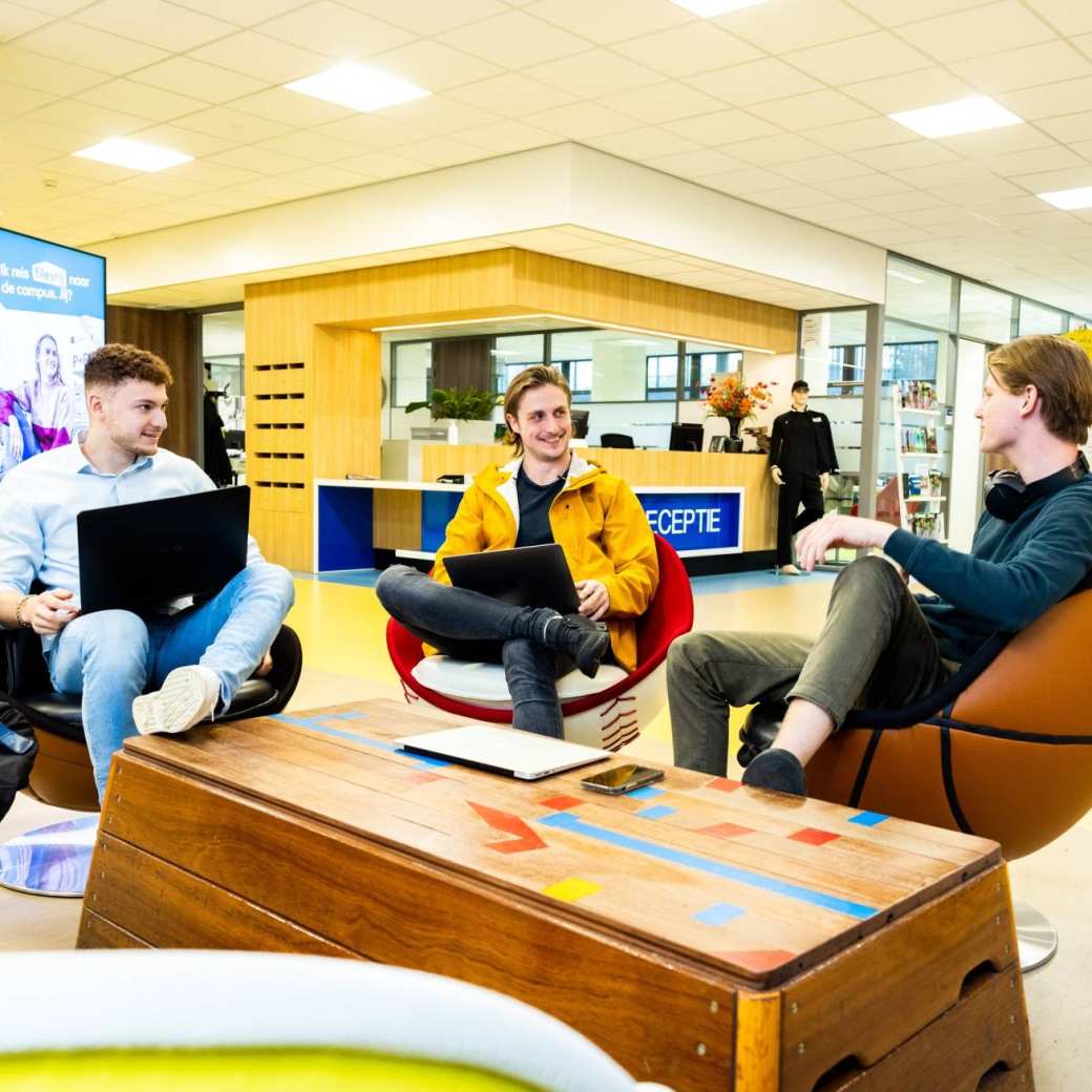 Stagiairs kletsen op draaistoelen in hal Gymnasion.