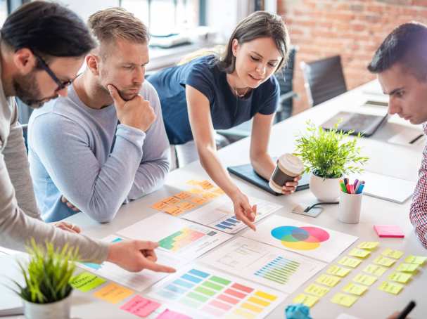 Sfeerbeeld van collega's die samenwerken aan een tafel met post-its, schema's en tabellen