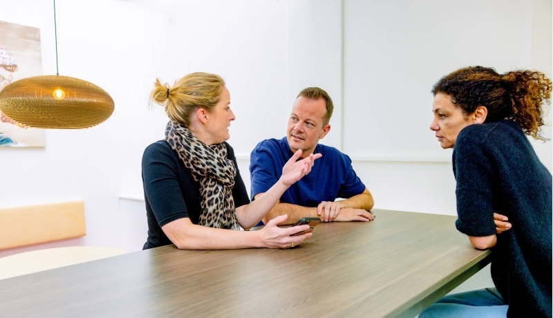 Vrouw legt iets uit aan man en vrouw tijdens de cursus acute pijn service. Dit doet ze in de kantine.