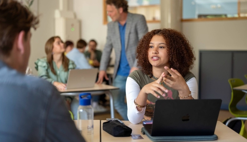 Meisje student in gesprek met jongen, in de klas, met laptop.