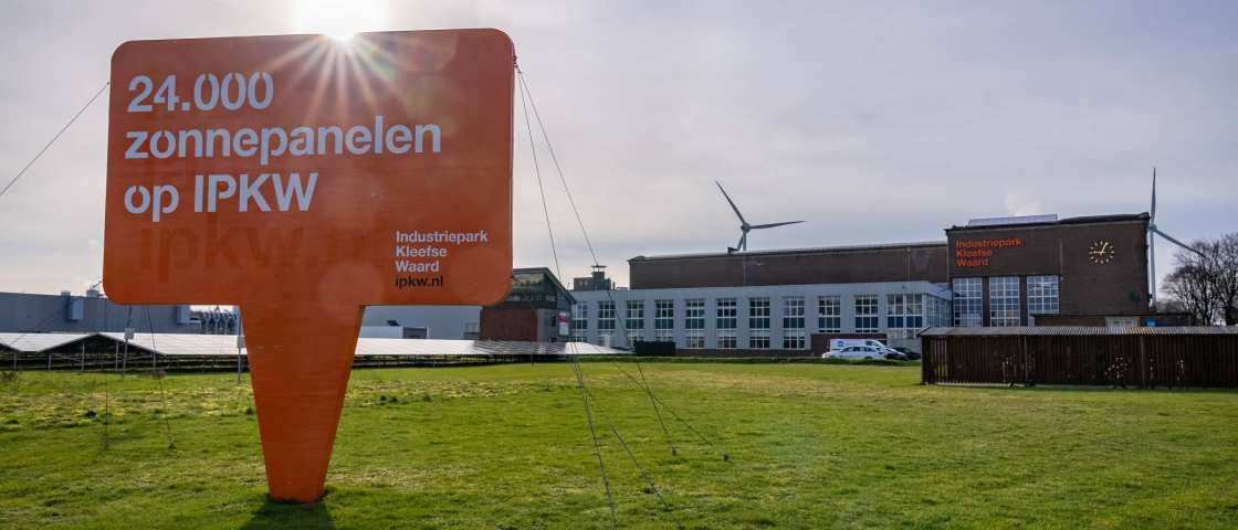 Foto van het Industriepark Kleefse Waard (IPKW) bij de ingang van het park met een informatiebord over zonnepanelen capaciteit van het IPKW op een grasgroene vlakte. Academie Engineering en Automotive.